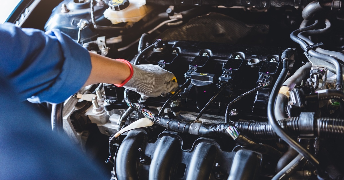 A close-up of a car mechanic's glove as they check under the hood and add oil in a vehicle at an auto repair shop.