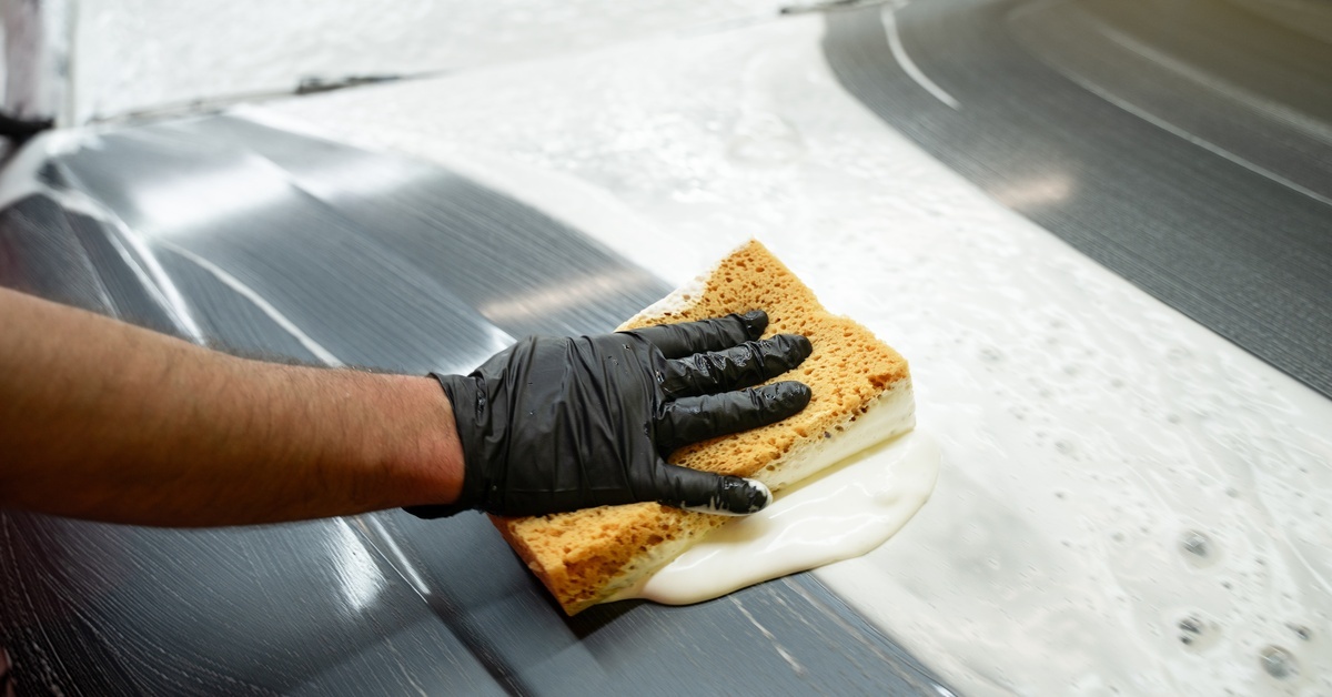 A close-up of someone's hand cleaning with a sponge. The water is soapy, and they're cleaning a stainless steel machine.