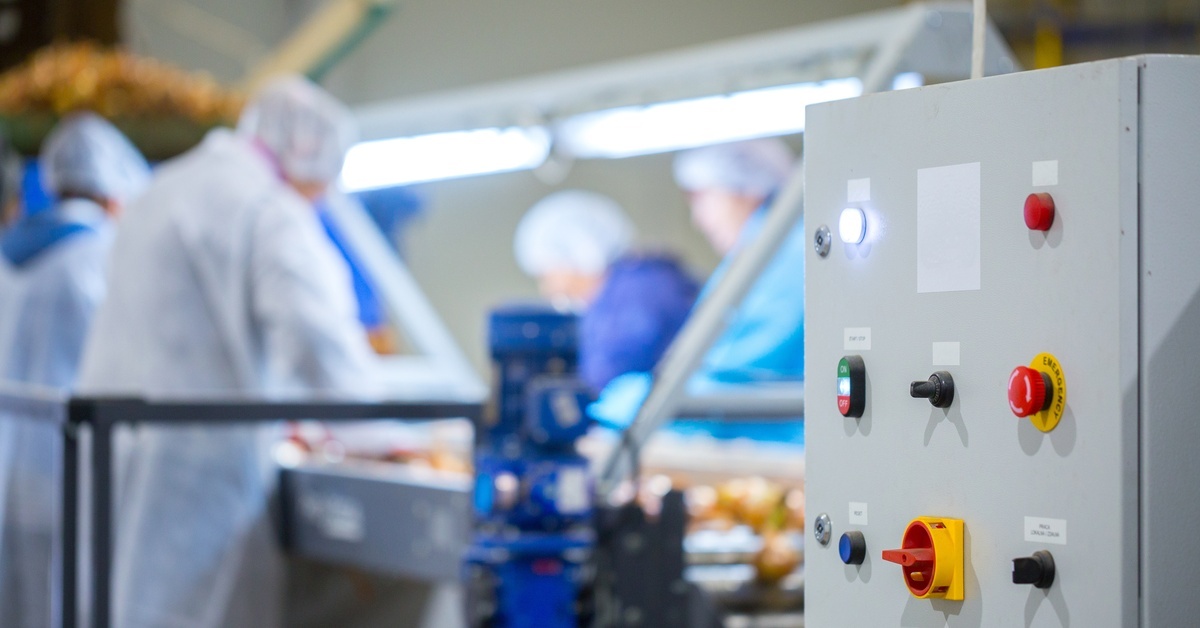 Close-up of a control panel on a conveyor used for storing crops or goods. Workers in the background are out of focus.