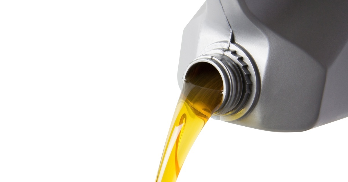 The Complete Maintenance Guide for Hydraulic Oil Close-up of pouring motor oil from a silver plastic gallon bottle into a grey canister with yellow petroleum liquid.