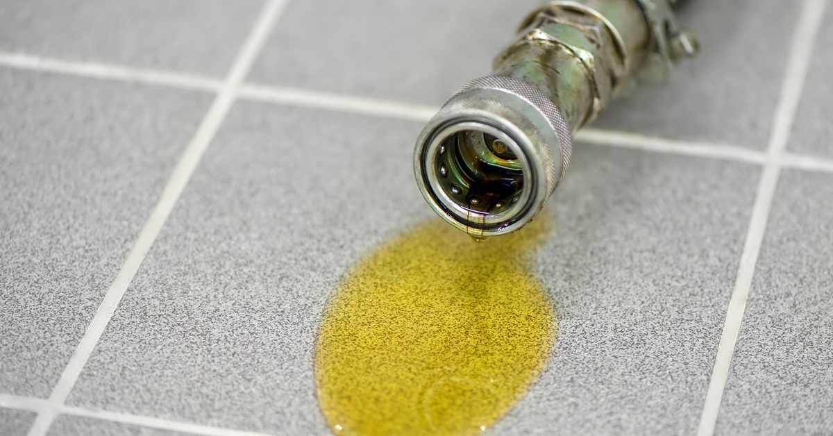 The Complete Maintenance Guide for Hydraulic Oil An extremely close-up of yellow hydraulic oil leaking out of a hydraulic hose on the gray tiled floor.