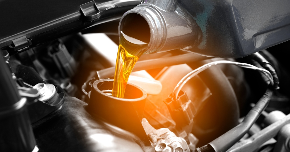 A close-up of a person refueling and pouring premium oil into the car's engine, transmission, and maintenance components.
