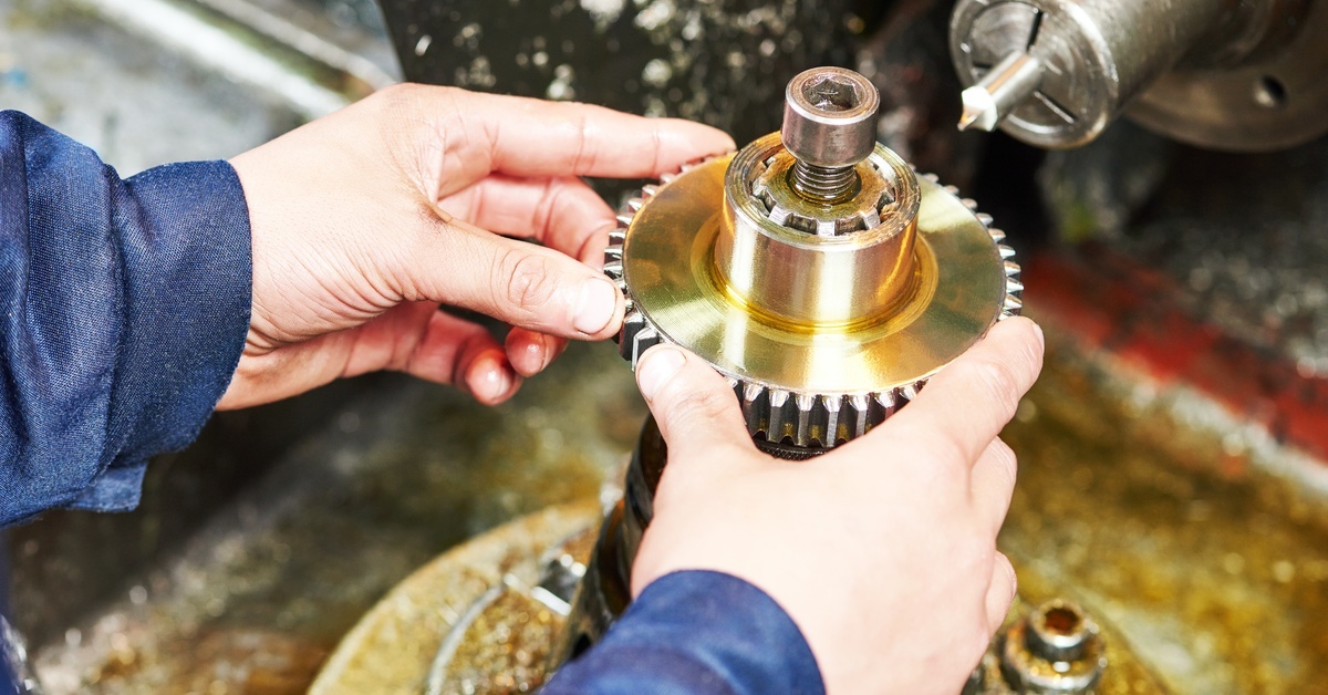 Comparing Synthetic and Biodegradable Oils A close-up of someone adding lubricant oil to a tooth gear wheel machining tool in an industrial room.