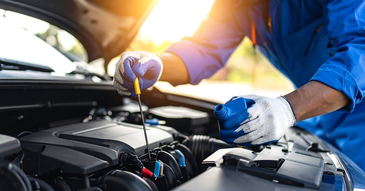 A close-up of a mechanic checking the engine oil level of a vehicle. They're wearing gloves and are using a metal stick.