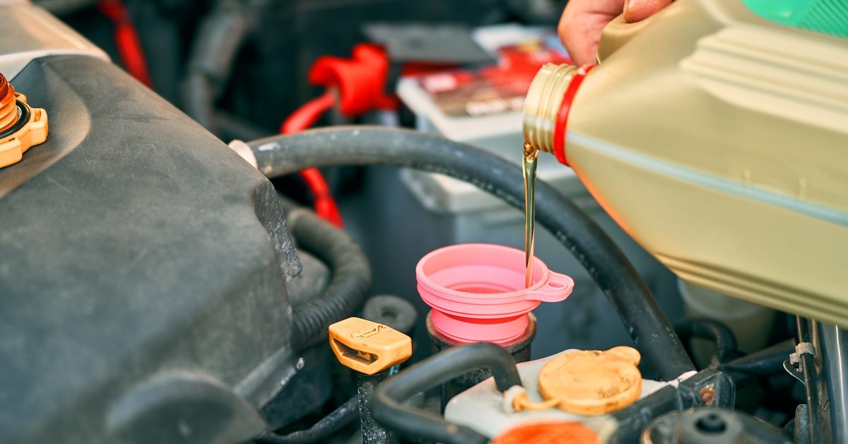 A close-up of someone pouring yellow-golden oil out of a golden container into a vehicle's motor engine.