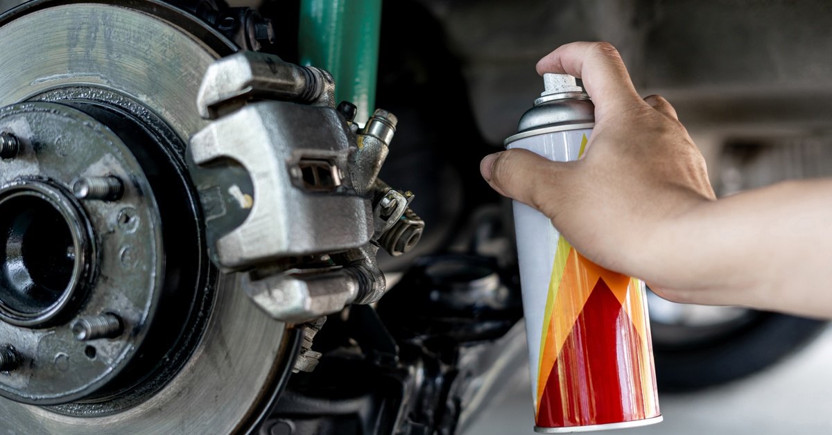 A close-up of someone's hand using a spray can to repair the car suspension and disk brake plate in a garage.