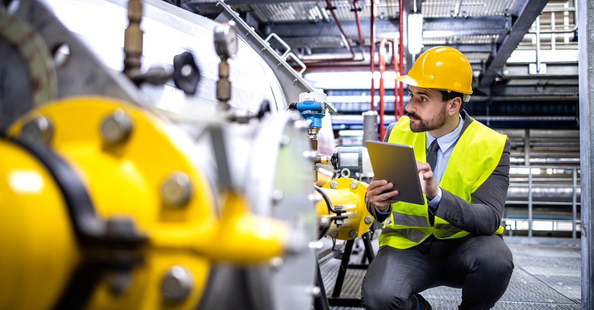 A close-up of an oil and gas production supervisor holding a digital tablet, inspecting the natural gas supply at a refinery.