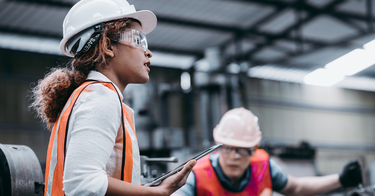 A close-up female industrial engineer wearing a white helmet while standing in a heavy industrial factory.