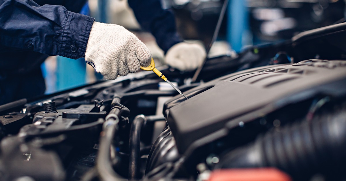 A close-up of an auto repair service center and a mechanic checking the engine oil level of a vehicle under the hood.