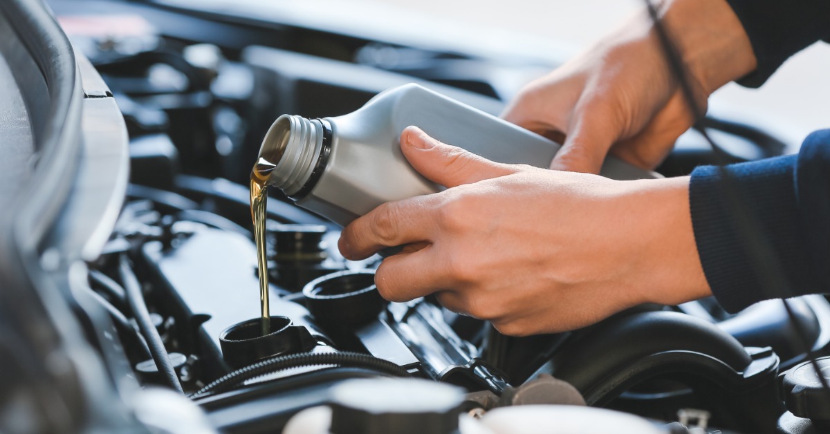 A close-up of a male professional mechanic refilling car oil out of a grey bottle in a service center.