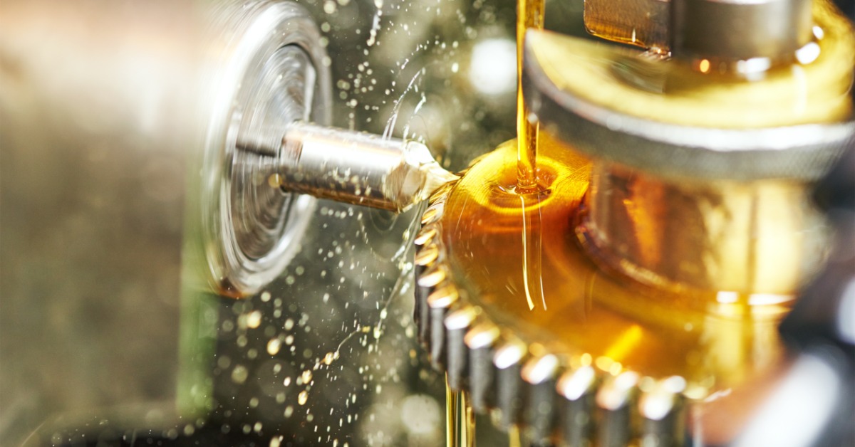 Industrial gear cutting process with rotating metal blank, coolant pouring over the tool and splashing outward.