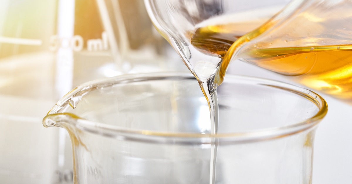 Amber chemical solution flows between glass beakers on a lab bench, with measurement markings visible nearby.