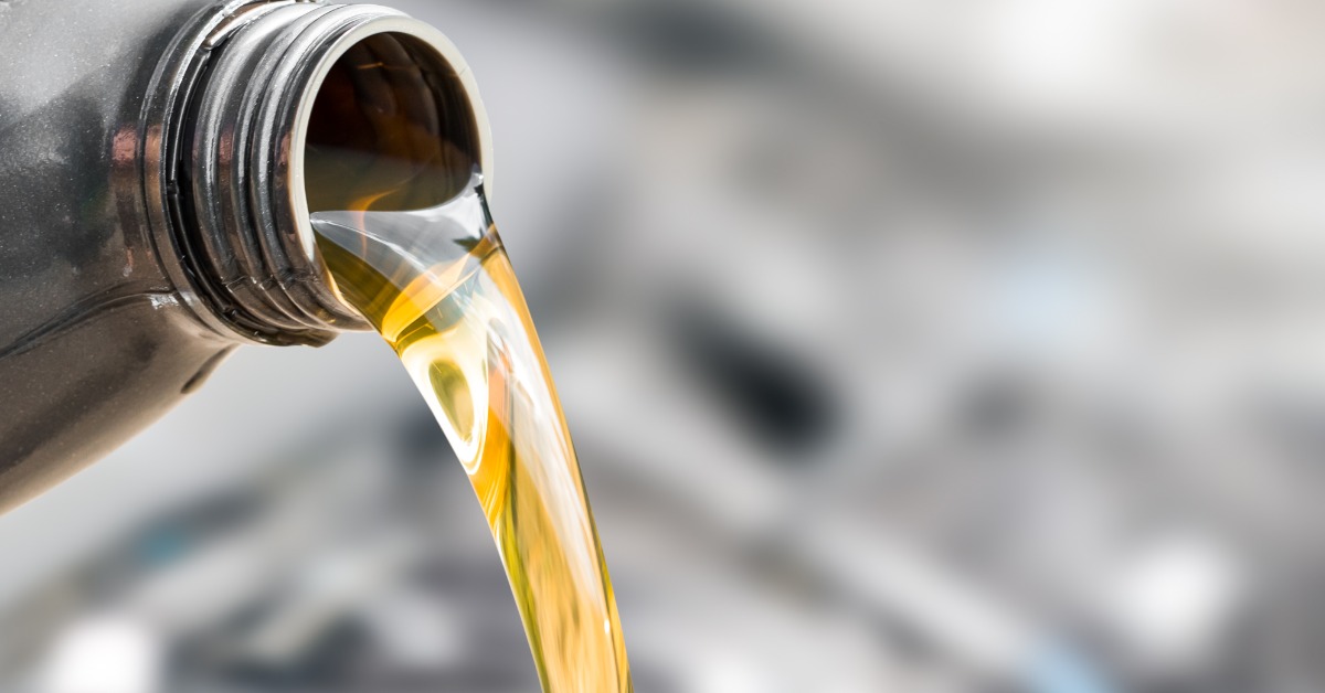 Close-up of motor oil pouring from a metal container spout, golden liquid flowing smoothly against a blurred background.