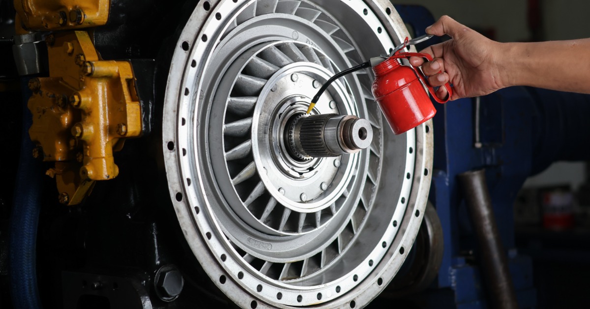 Hand uses a red oil can to lubricate the central shaft of a large circular turbine or engine component.