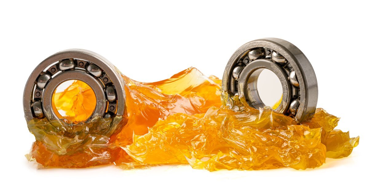 Close-up of two ball bearings resting in glossy orange lubricant, with metal rings and bearing balls exposed.