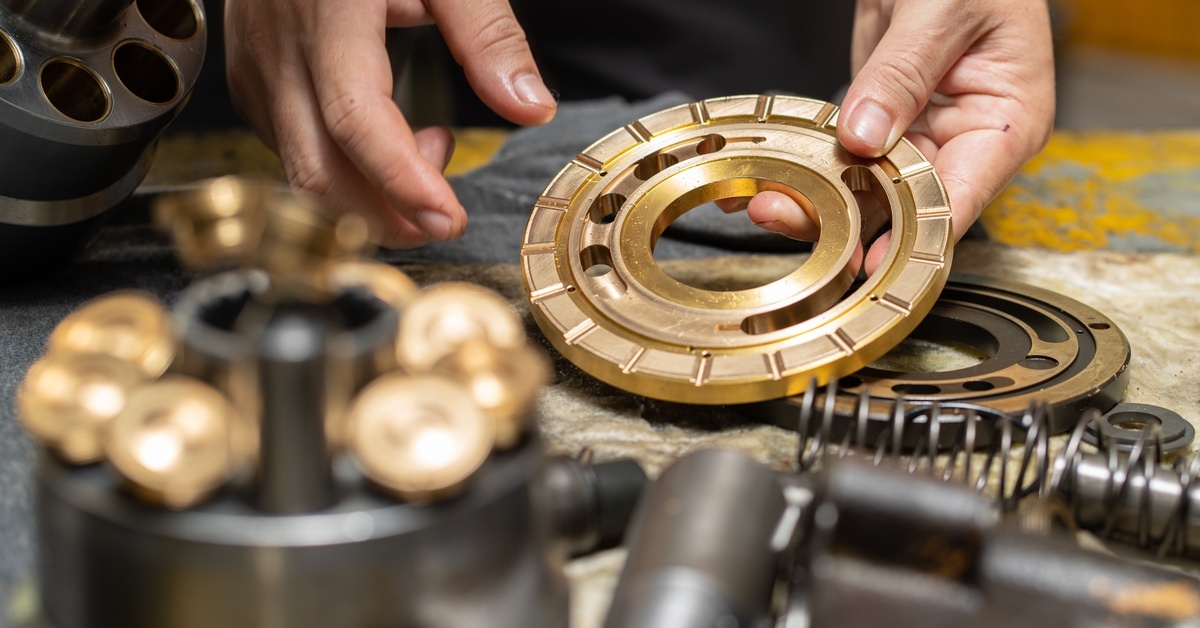 Close-up of hands inspecting a machined metal ring beside disassembled mechanical components on a workbench.