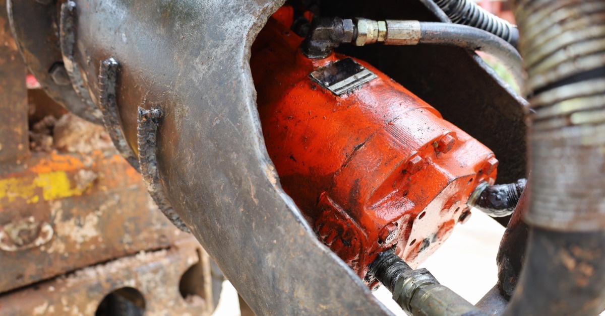 Red hydraulic motor with attached hoses installed inside heavy equipment, showing wear from industrial use