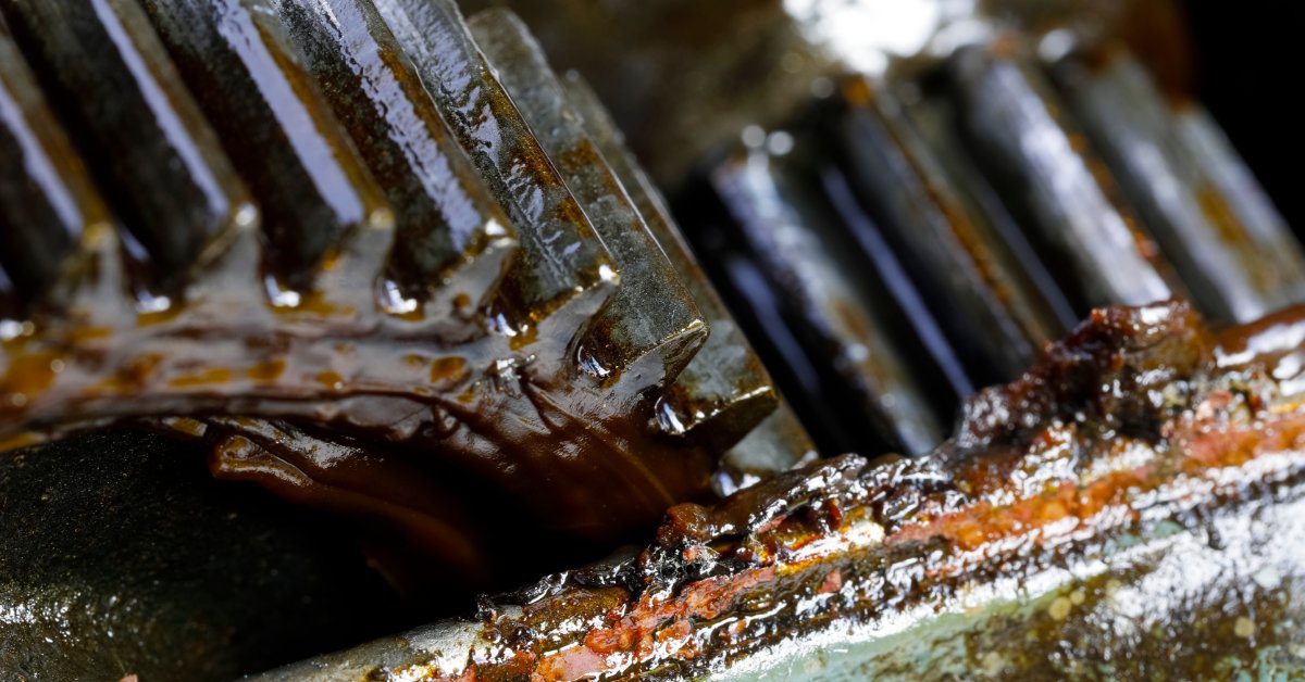 Why Degreasing Is Critical Before Lubricant Application Grease-covered metal gear teeth mesh inside industrial machinery, with rust and residue visible along the edges.