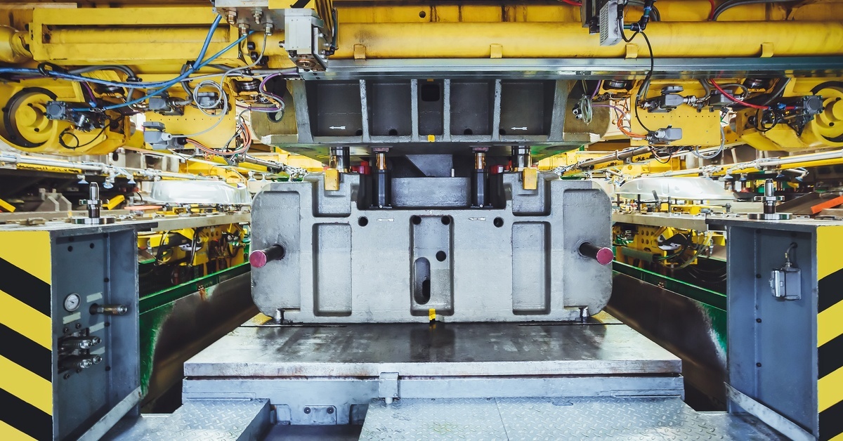 The inside of a large industrial hydraulic press with yellow metal pipes in a manufacturing facility.