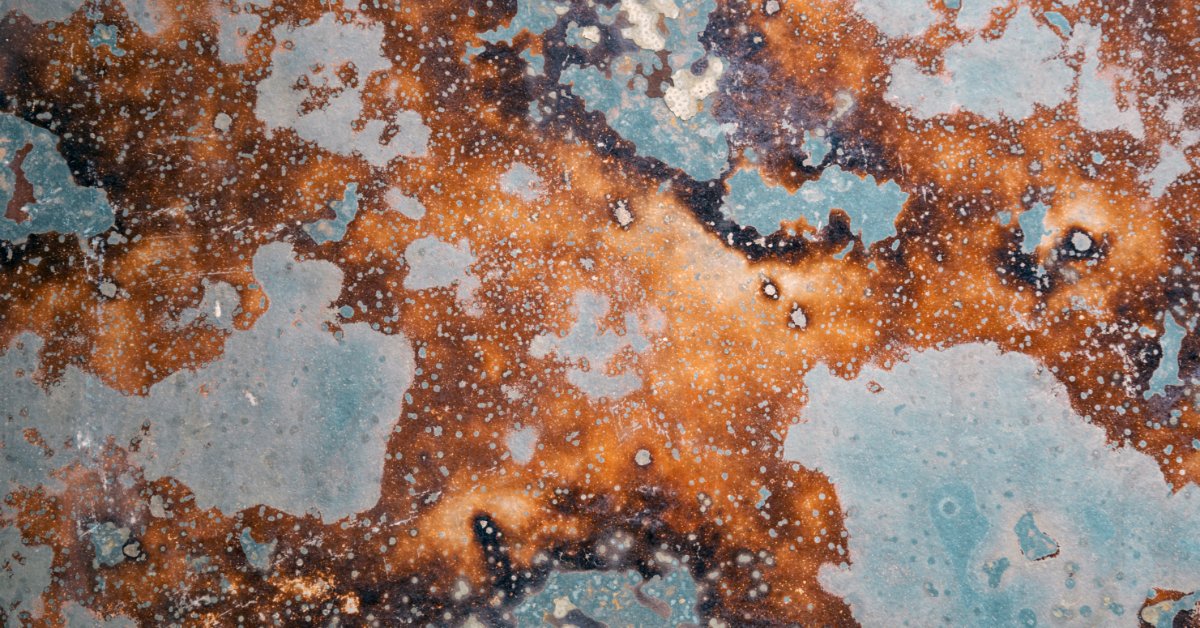A vintage metal plate shows rusted blue, brown, and orange corrosion across its weathered surface.