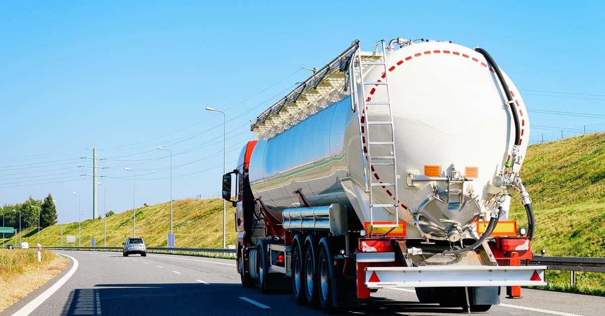 A driver maneuvering a white tanker truck down a highway, delivering bulk fuel across smooth asphalt roads.