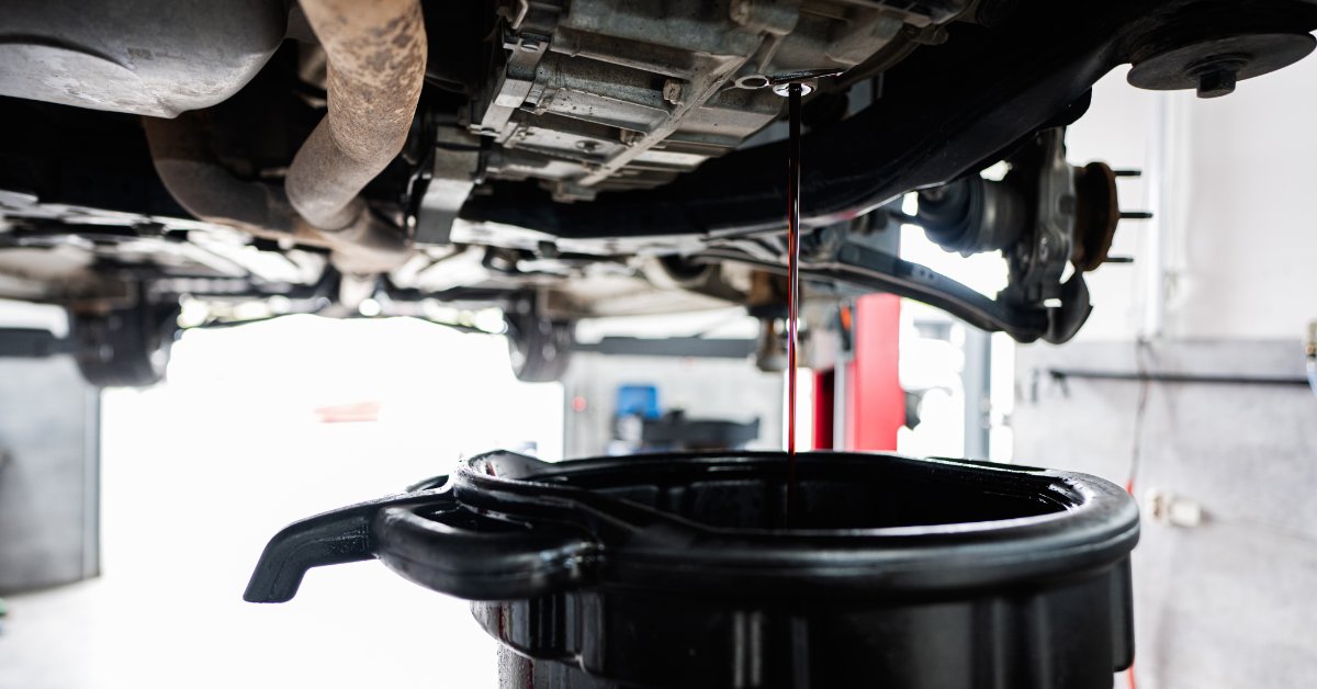 How Automotive Lubricants Help Reduce Emissions Dark motor oil drains from a raised vehicle into a collection pan. The vehicle's undercarriage parts are above the pan.