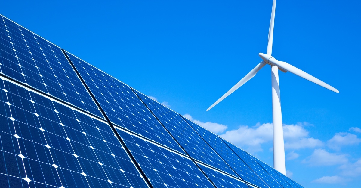 Multiple black and metallic solar panels, up close, and a white wind turbine standing tall against a blue sky.