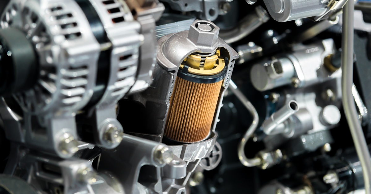 A vehicle's engine oil filter is a light brown color and visibly dirty. Other engine components surround it.