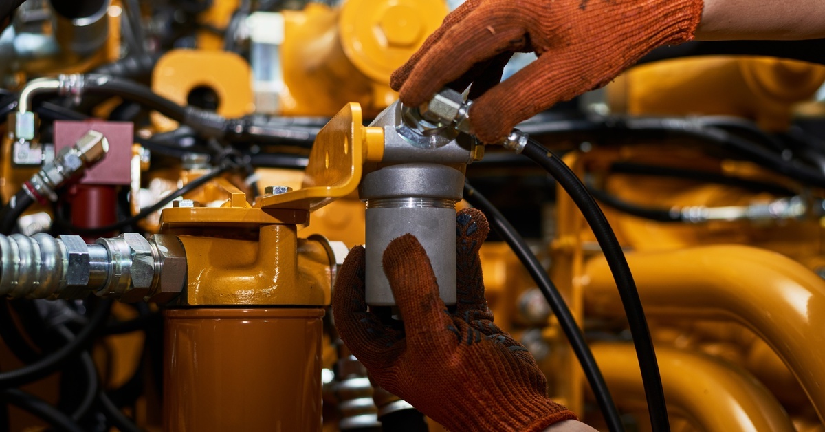 A mechanic inspects hydraulic pipes on heavy machinery to ensure proper maintenance and system function.