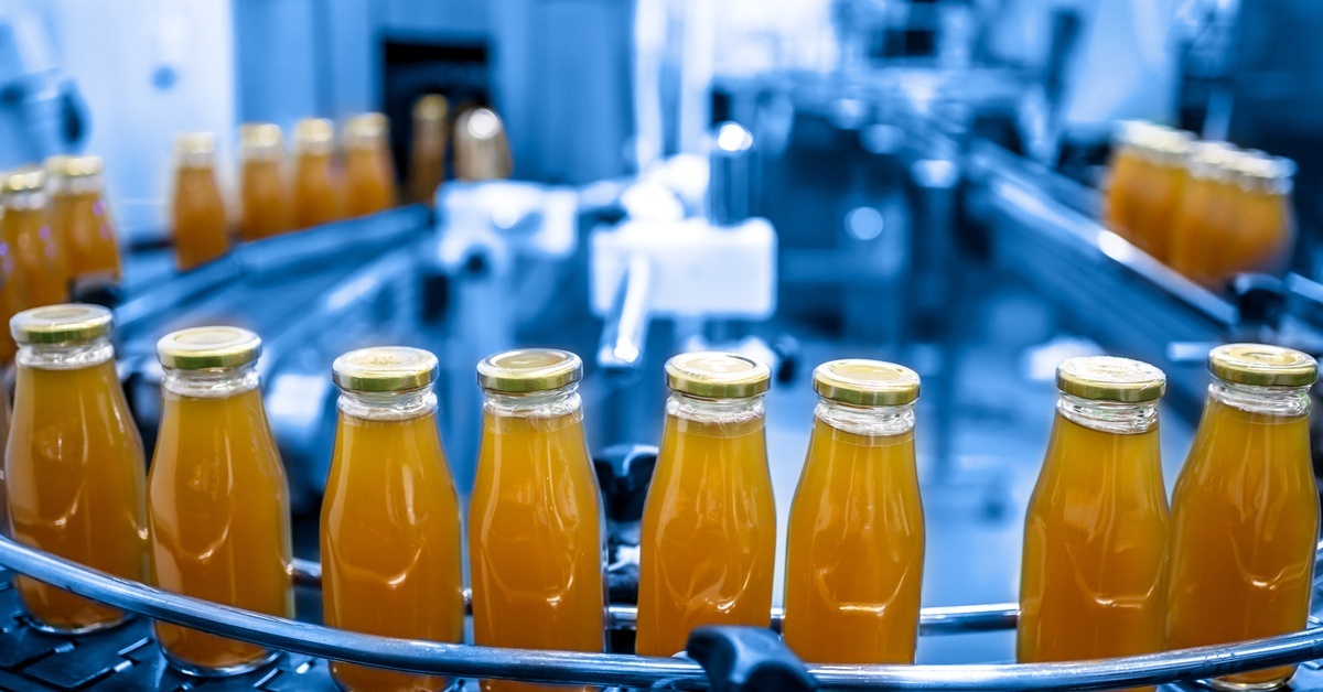 Juice bottles with screw caps move along a long conveyor belt in a beverage factory&rsquo;s production line.