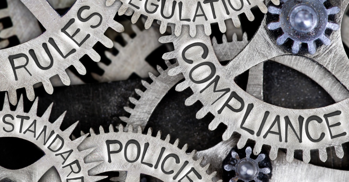 Multiple metallic gear wheels interlock, displaying the engraved words 'compliance' and 'rules'.