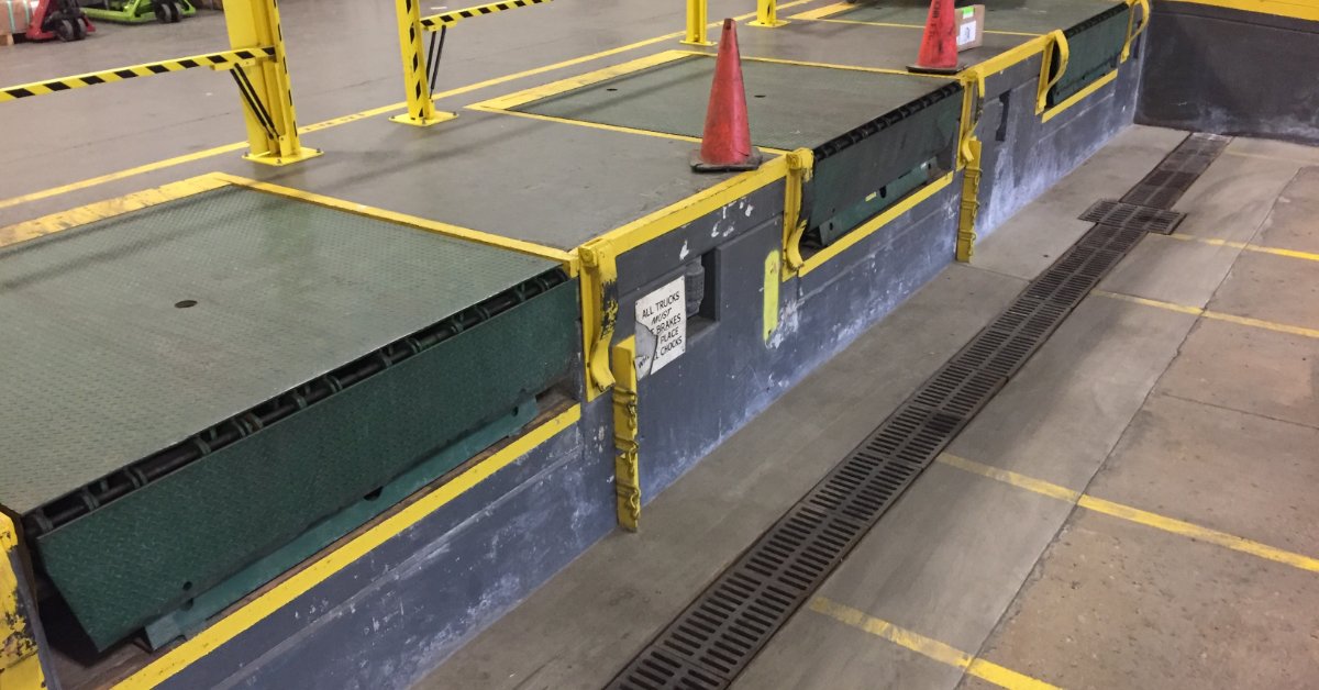 Using Degreasers in Pressure Washing Applications A warehouse loading area contains a green loading platform bordered by yellow metal barriers with black safety stripes.