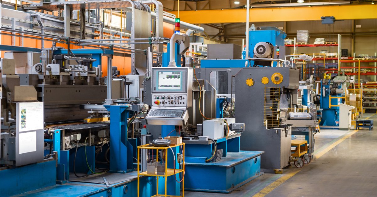 Using Degreasers in Pressure Washing Applications A large industrial manufacturing facility contains blue and gray machinery, metal pipes, and overhead ductwork.