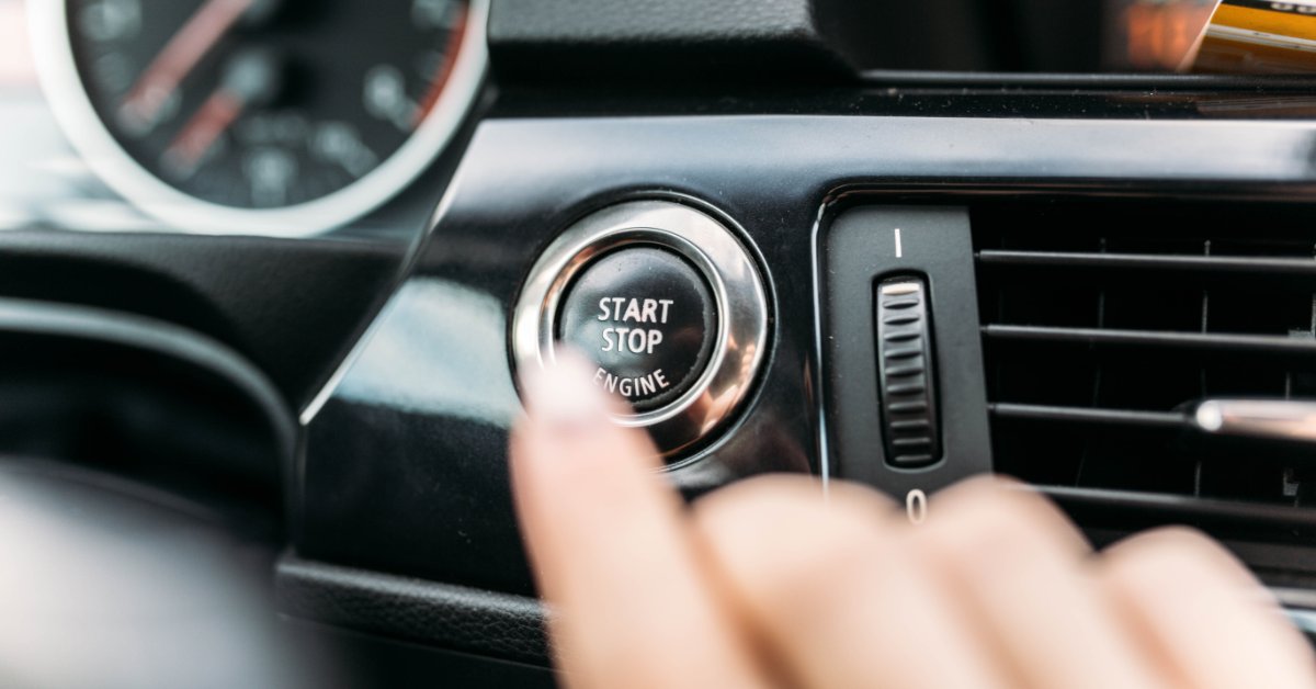 Comparing Conventional and Synthetic Blend Oils A person reaches toward a circular start/stop engine button inside a car. Part of the gauge cluster is visible.